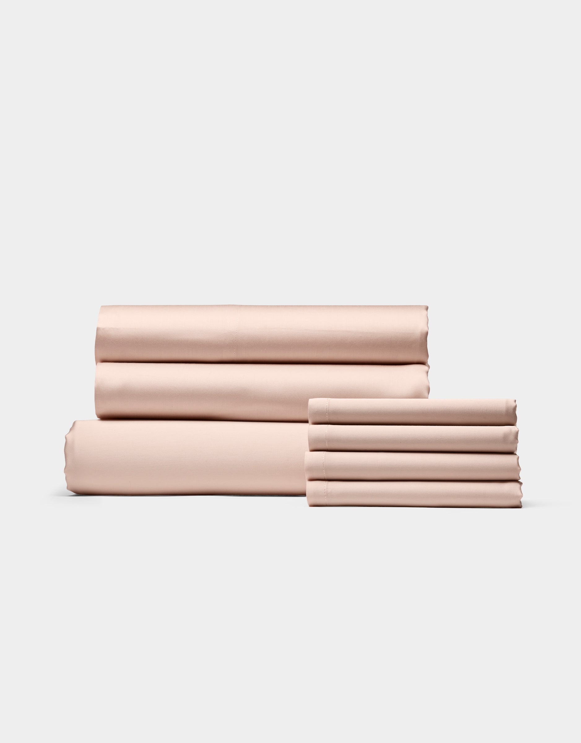 Cozy Earth’s Bamboo Bedding Core Bundle, shown in light pink, features neatly folded bed sheets and pillowcases arranged in two stacks against a simple, light background.|Color:Peony