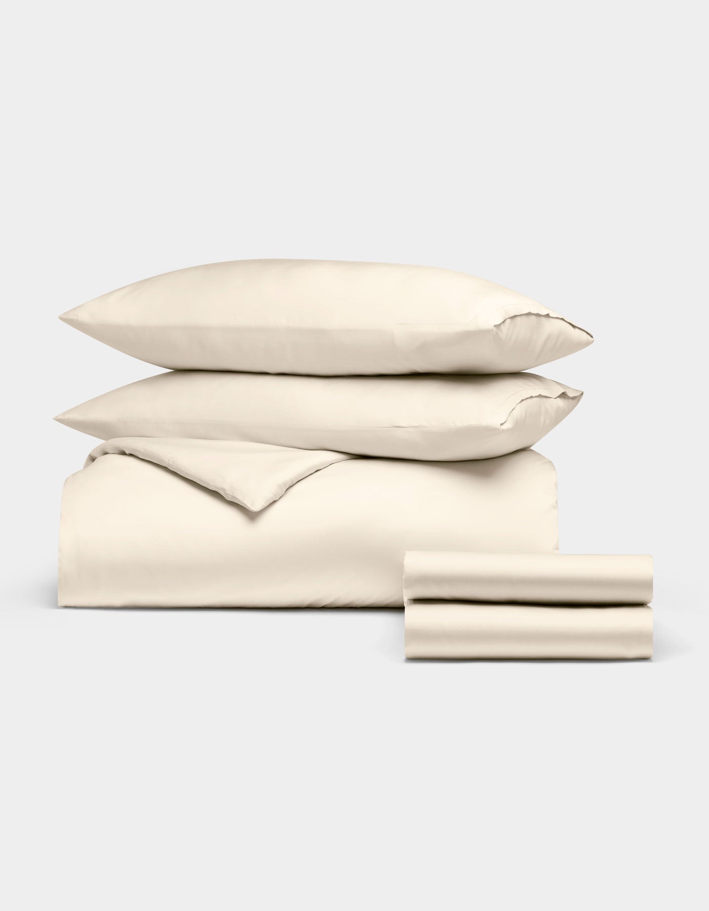 The Cozy Earth Bamboo Bedding Deluxe Bundle, featuring a cream comforter, two pillows, and two stacked sheets, is neatly folded and displayed against a plain light gray background.|Color:Creme