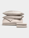 The Cozy Earth Bamboo Bedding Deluxe Bundle features two stacked pillows, a comforter, and folded sheets in cream, all neatly arranged against a plain white background.|Color:Driftwood