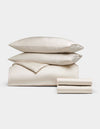 Cozy Earth's Bamboo Bedding Deluxe Bundle, featuring two pillows, a folded comforter, and two folded sheets in cream, is neatly stacked and displayed on a plain white background.|Color:Oat