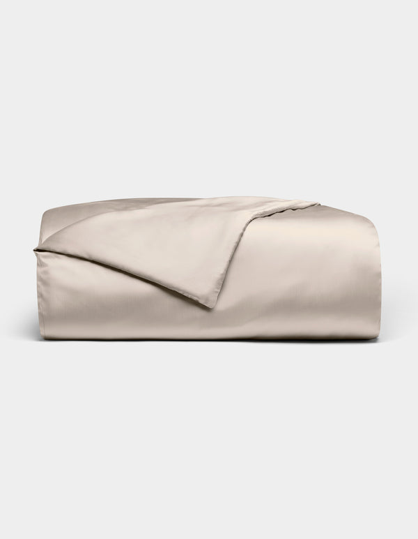 The Bamboo Duvet Cover by Cozy Earth is shown neatly folded in light beige with a smooth, shiny finish against a white background; one corner is flipped open to reveal the inner side.|Color:Driftwood