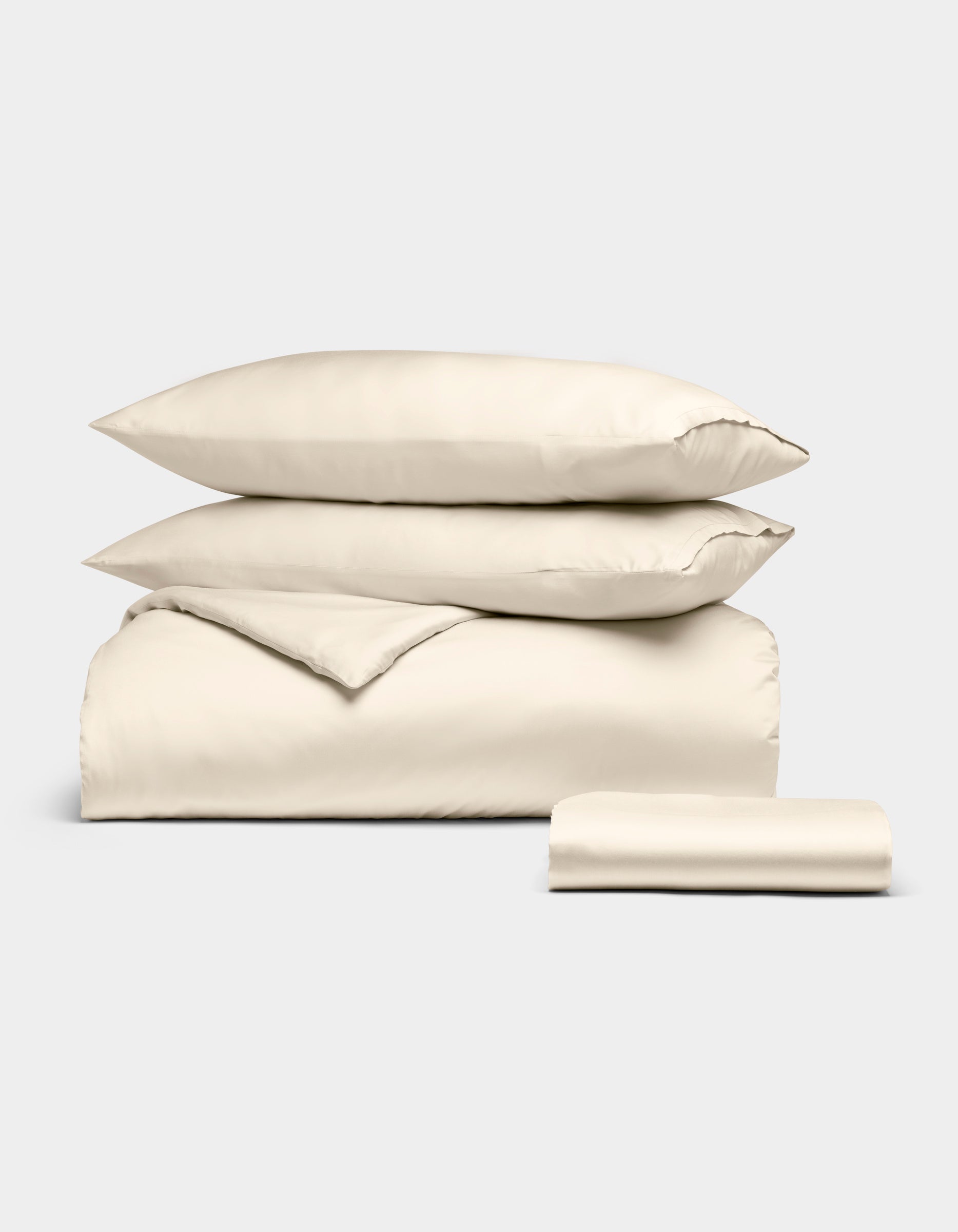 The Cozy Earth Bamboo Bedding Essential Bundle, featuring a cream-colored duvet cover, two pillowcases, and a flat sheet, is neatly folded and displayed against a plain white background.|Color:Creme