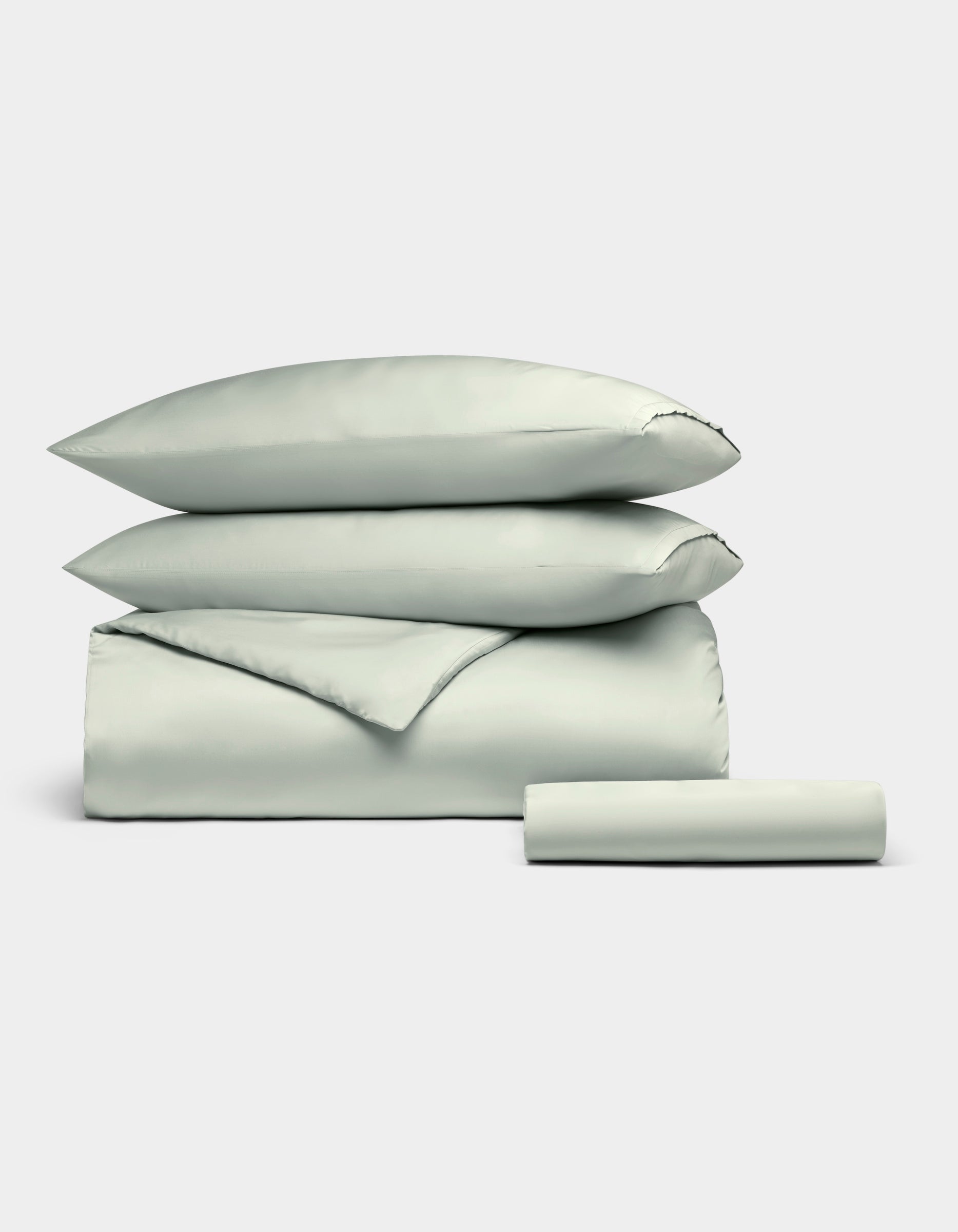 The Cozy Earth Bamboo Bedding Essential Bundle, featuring two pillows, a folded duvet, and a sheet in pale gray, is neatly stacked against a plain white background.|Color:Laurel