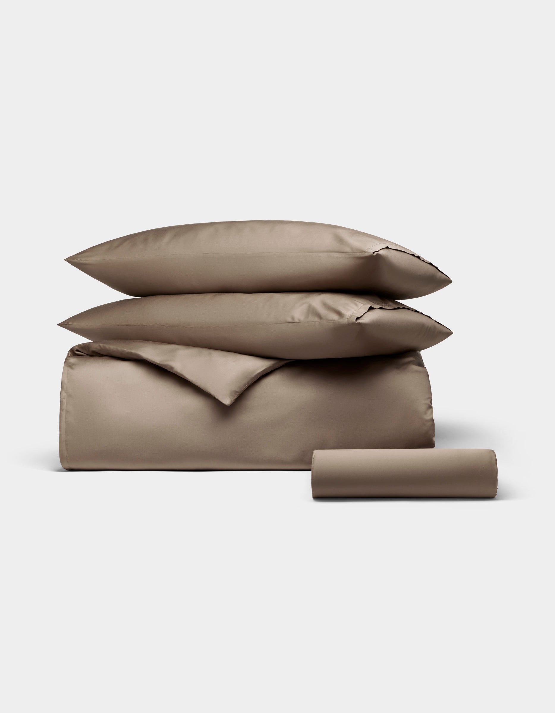 The Cozy Earth Bamboo Bedding Essential Bundle, featuring two pillows, a duvet cover, and a cylindrical bolster in taupe, is neatly folded and displayed against a plain light gray background.|Color:Walnut