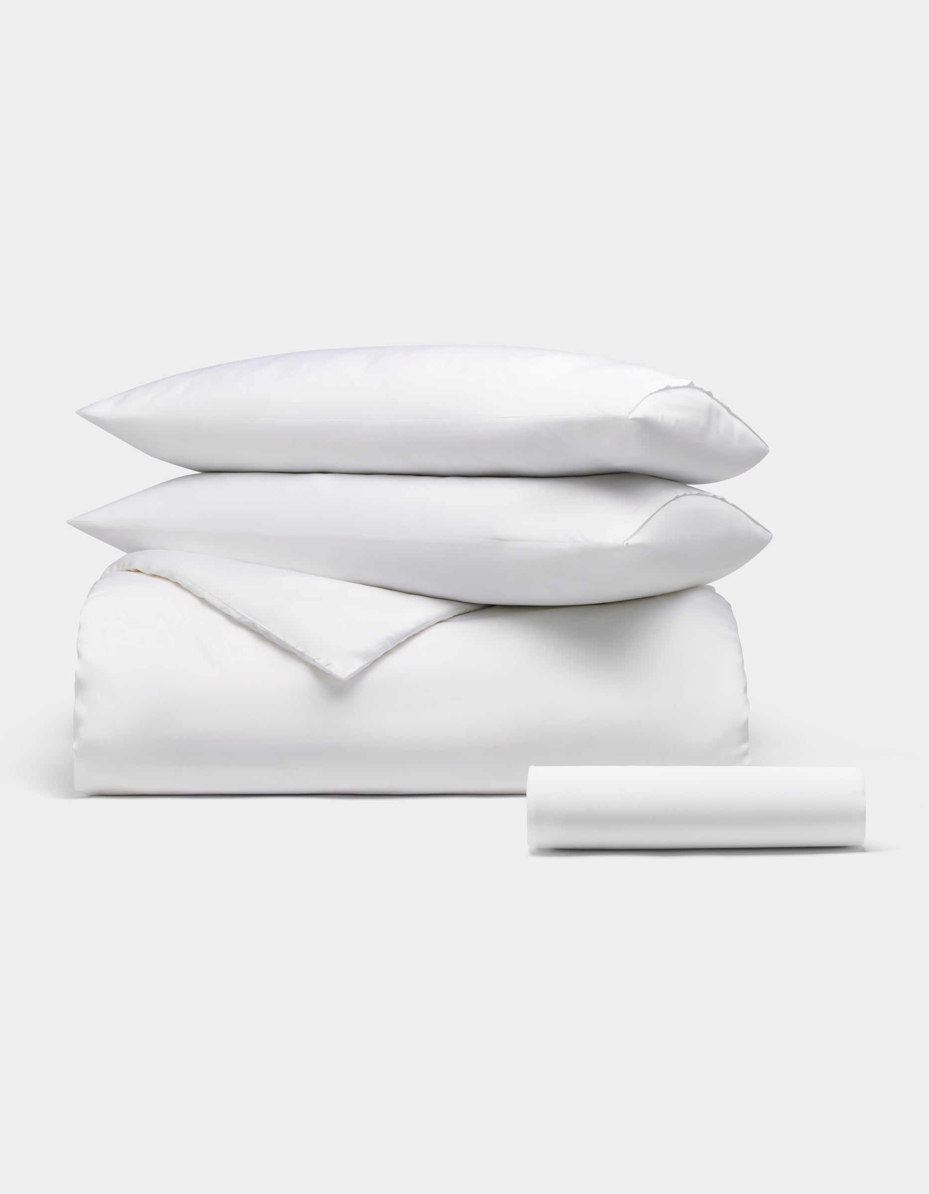 The Cozy Earth Bamboo Bedding Essential Bundle is neatly displayed: two pillows stacked on a folded comforter, with a rolled bedsheet in front, all set against a plain light background.|Color:White