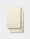 A folded Cozy Earth Silk Pillowcase in beige is stacked on a light gray background. |Color:Creme