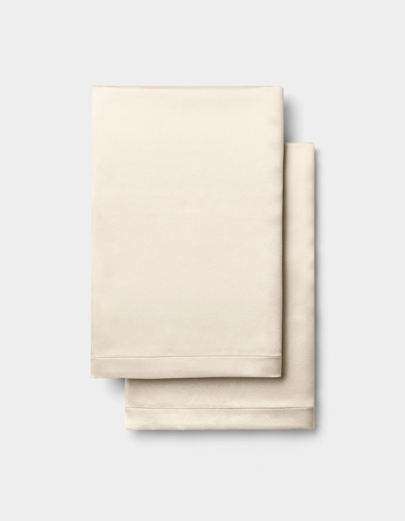 A folded Cozy Earth Silk Pillowcase in beige is stacked on a light gray background. |Color:Creme
