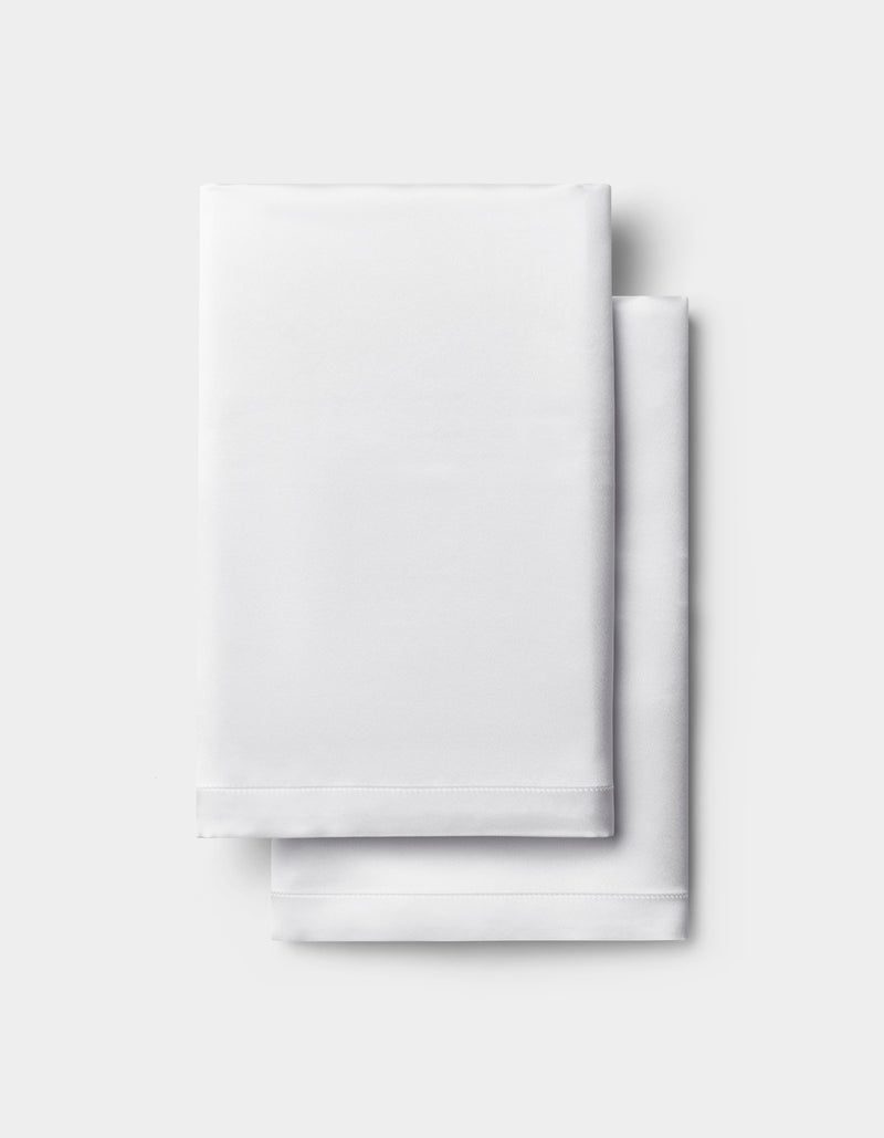 A neatly folded white Silk Pillowcase by Cozy Earth is stacked on a light gray background.