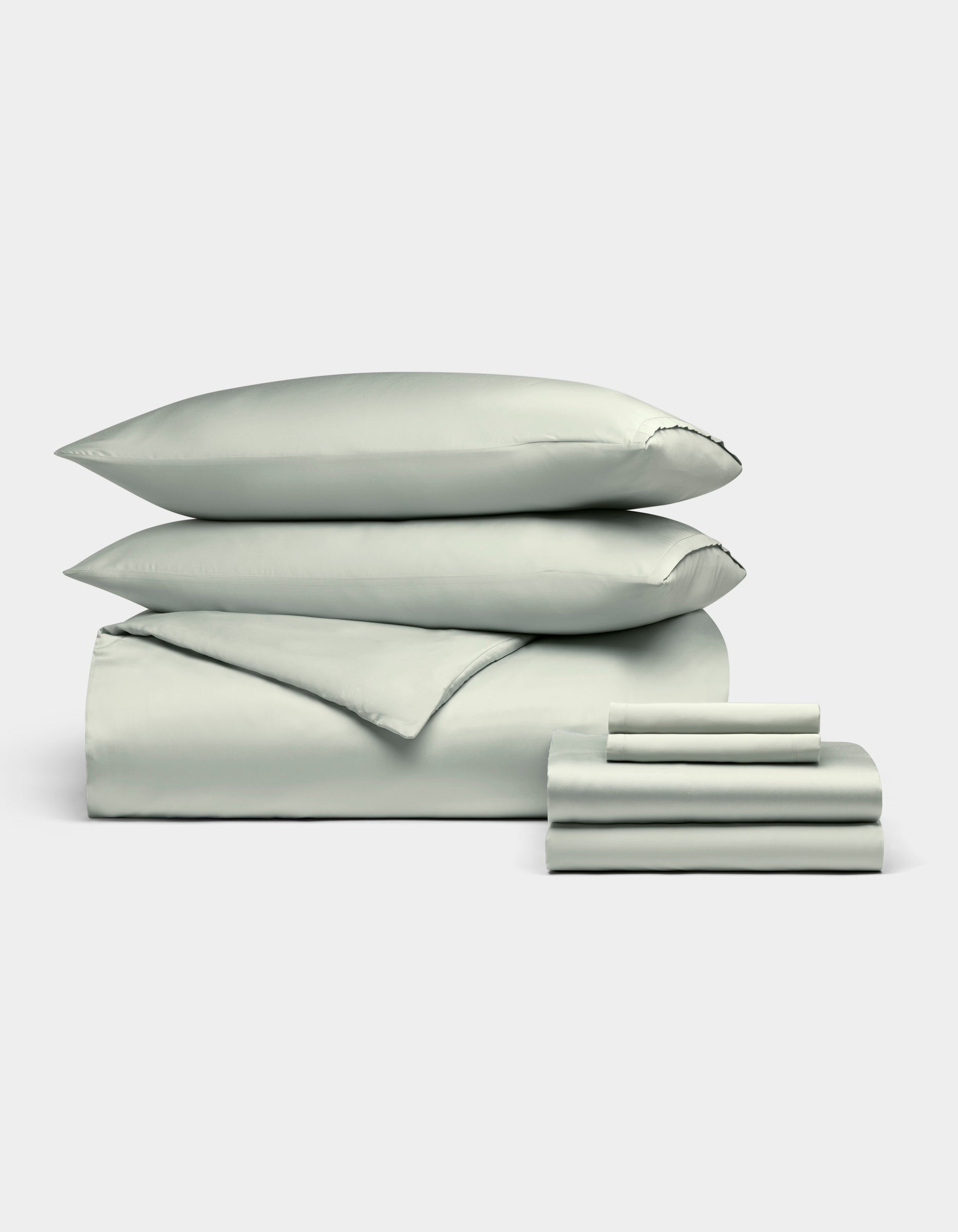A neatly stacked Cozy Earth Bamboo Bedding Ultimate Bundle, featuring two pillows, a folded duvet, and folded sheets in pale green, displayed against a plain white background.|Color:Laurel
