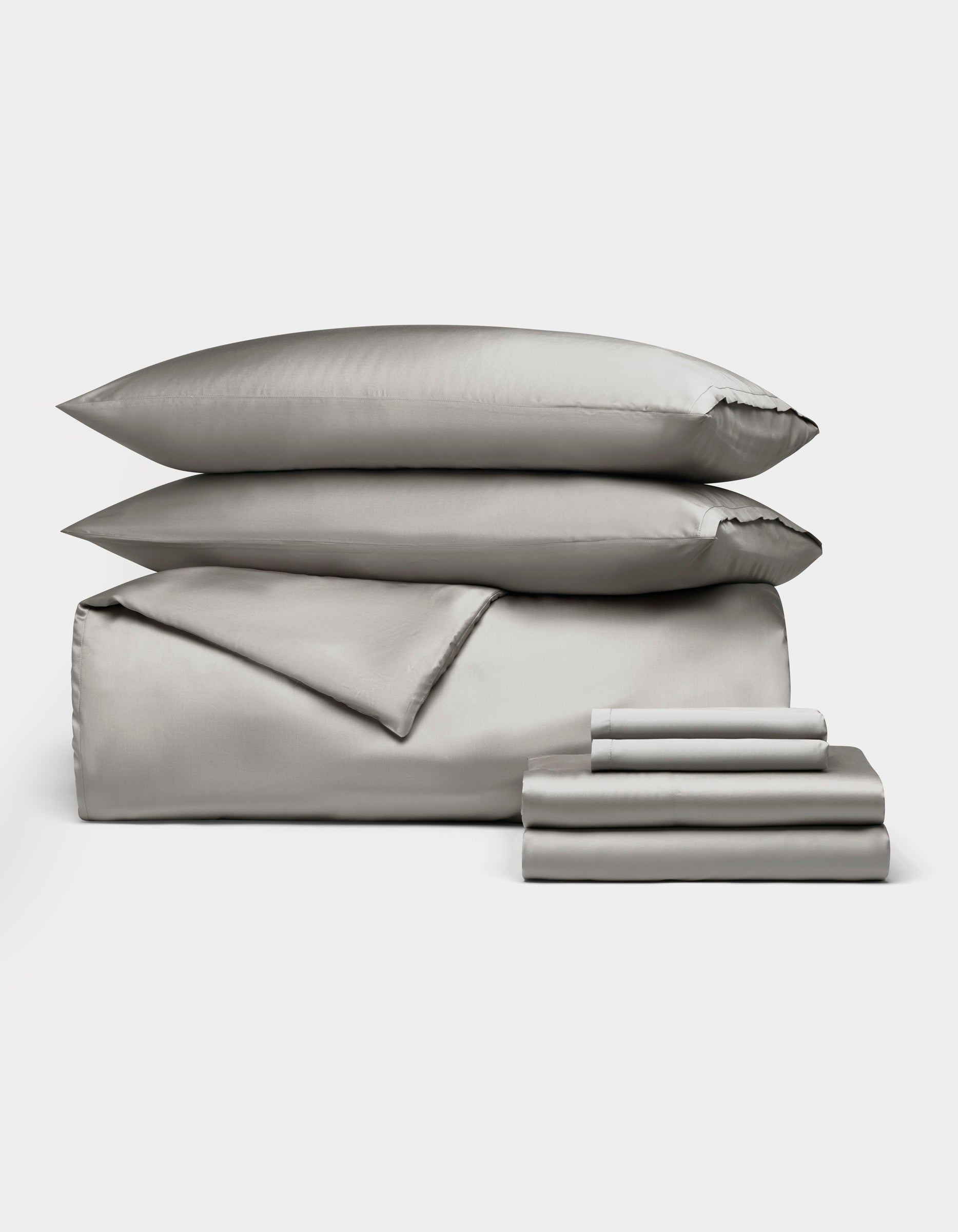 The Bamboo Bedding Ultimate Bundle by Cozy Earth features elegant silver-gray bedding, including two pillows, a comforter, and folded sheets, all neatly displayed against a plain white background.
