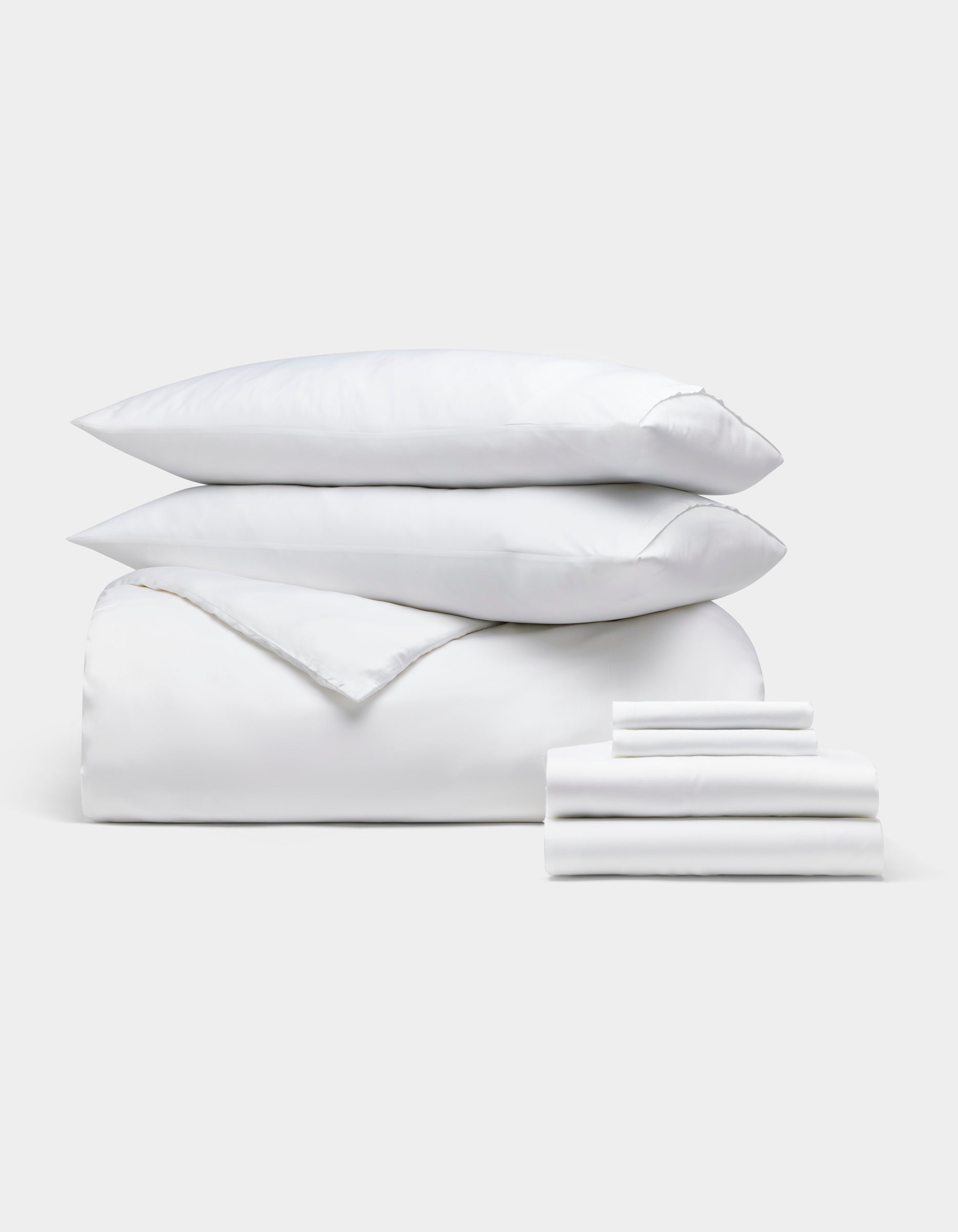 The Cozy Earth Bamboo Bedding Ultimate Bundle, featuring two pillows stacked on a comforter and folded sheets, is neatly displayed against a plain light gray background.