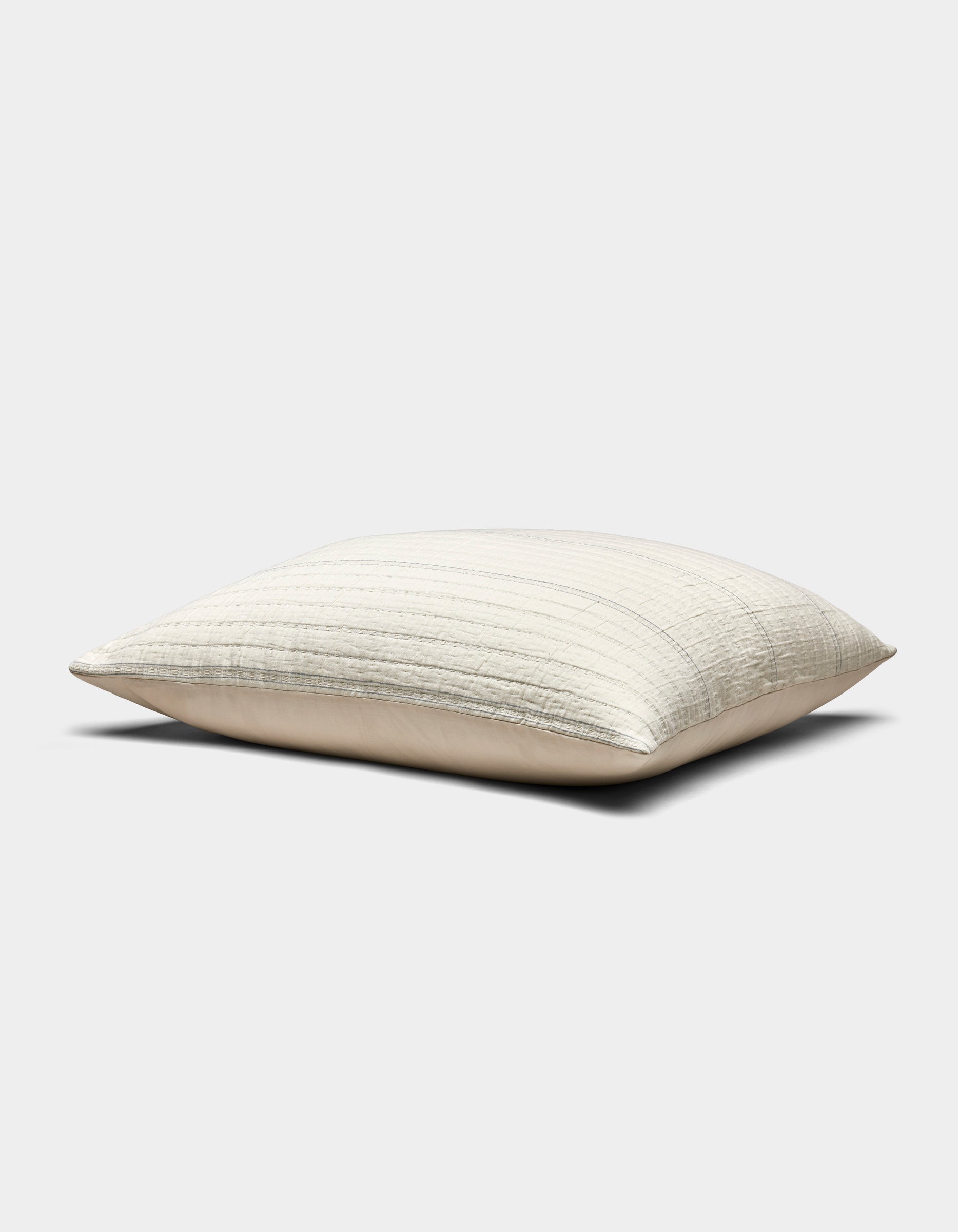 The Baja Matelasse Sham by Cozy Earth is a rectangular, light beige pillow with a subtle striped texture, pictured resting on a flat surface against a plain white background.|Color:Alabaster/Oceanside