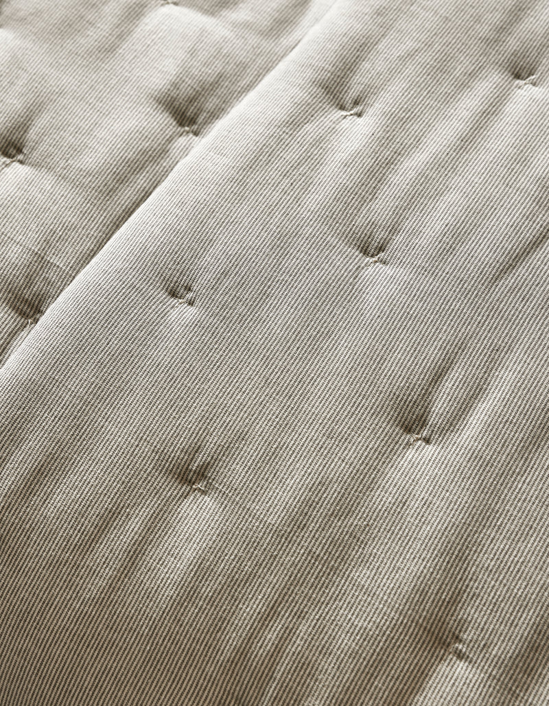 Close-up of the Cozy Earth Baja Quilt’s beige, textured surface featuring parallel lines and button-like tufts for a quilted, cushioned look.