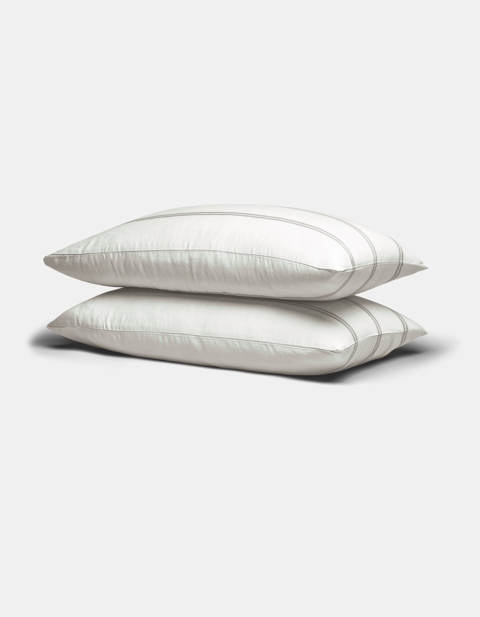 Two Bamboo Sheet Sets by Cozy Earth in white with subtle gray stripes, neatly stacked against a plain, light gray background.