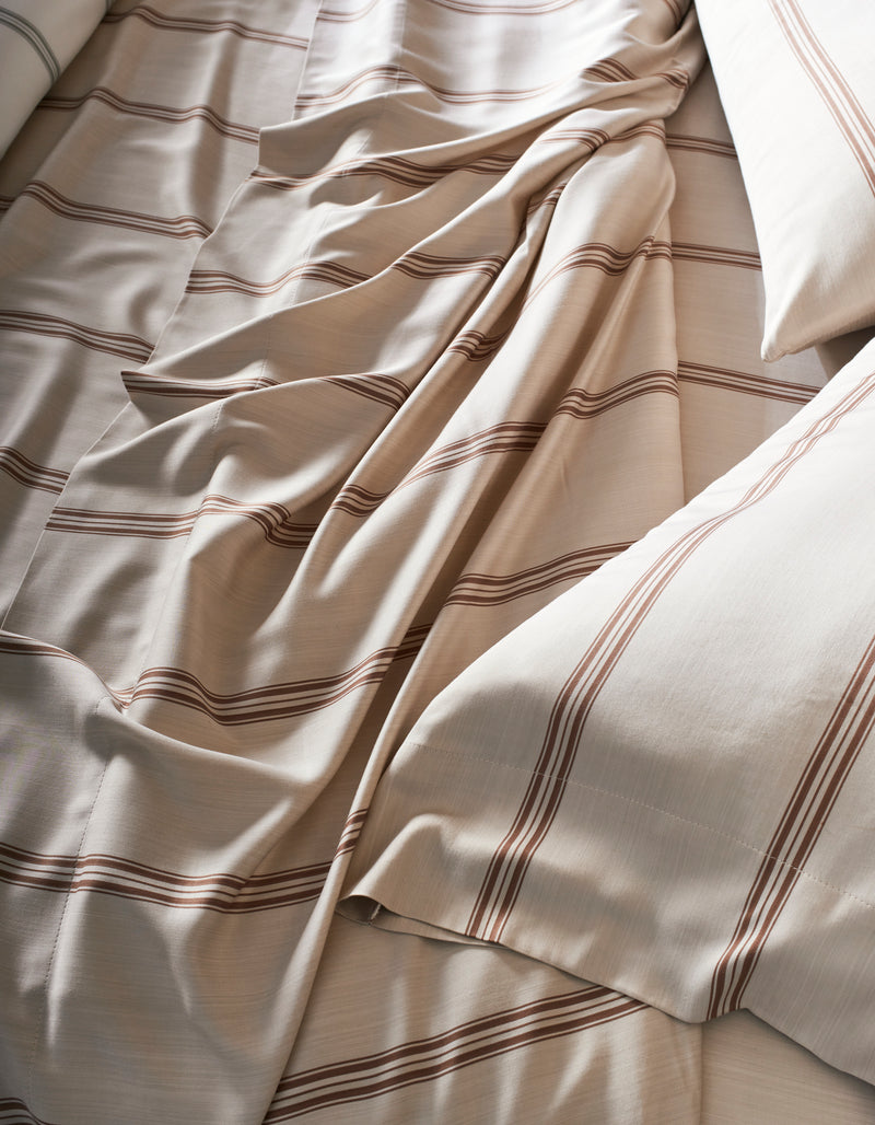 A close-up of the Cozy Earth Bamboo Sheet Set shows cream-colored sheets with brown horizontal stripes, slightly rumpled, and two pillows placed on either side.