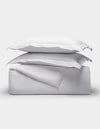 The Linen Duvet Set by Cozy Earth is shown neatly folded with two stacked pillows, arranged on top of folded sheets against a plain light background.|Color:White