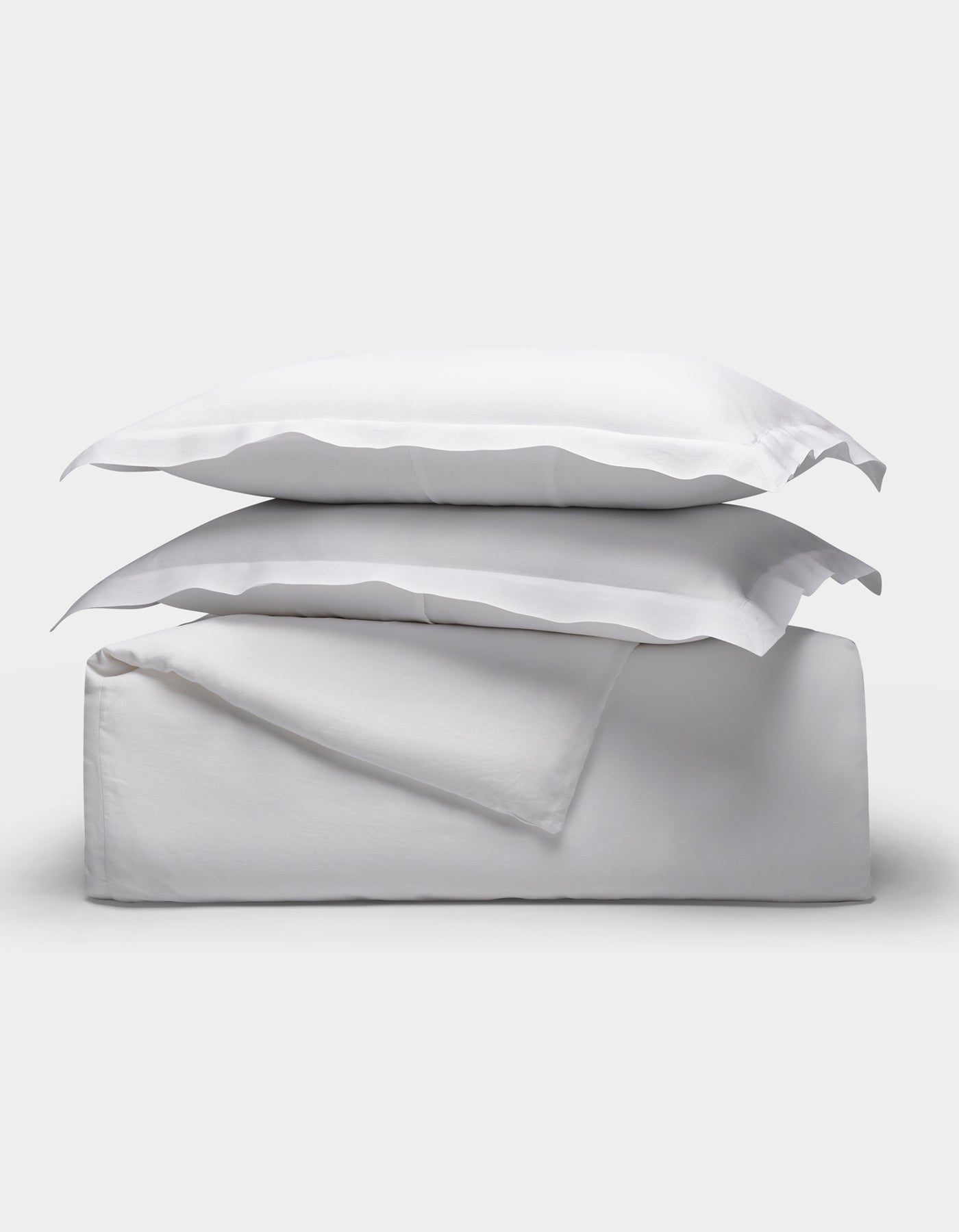 The Linen Duvet Set by Cozy Earth is shown neatly folded with two stacked pillows, arranged on top of folded sheets against a plain light background.|Color:White