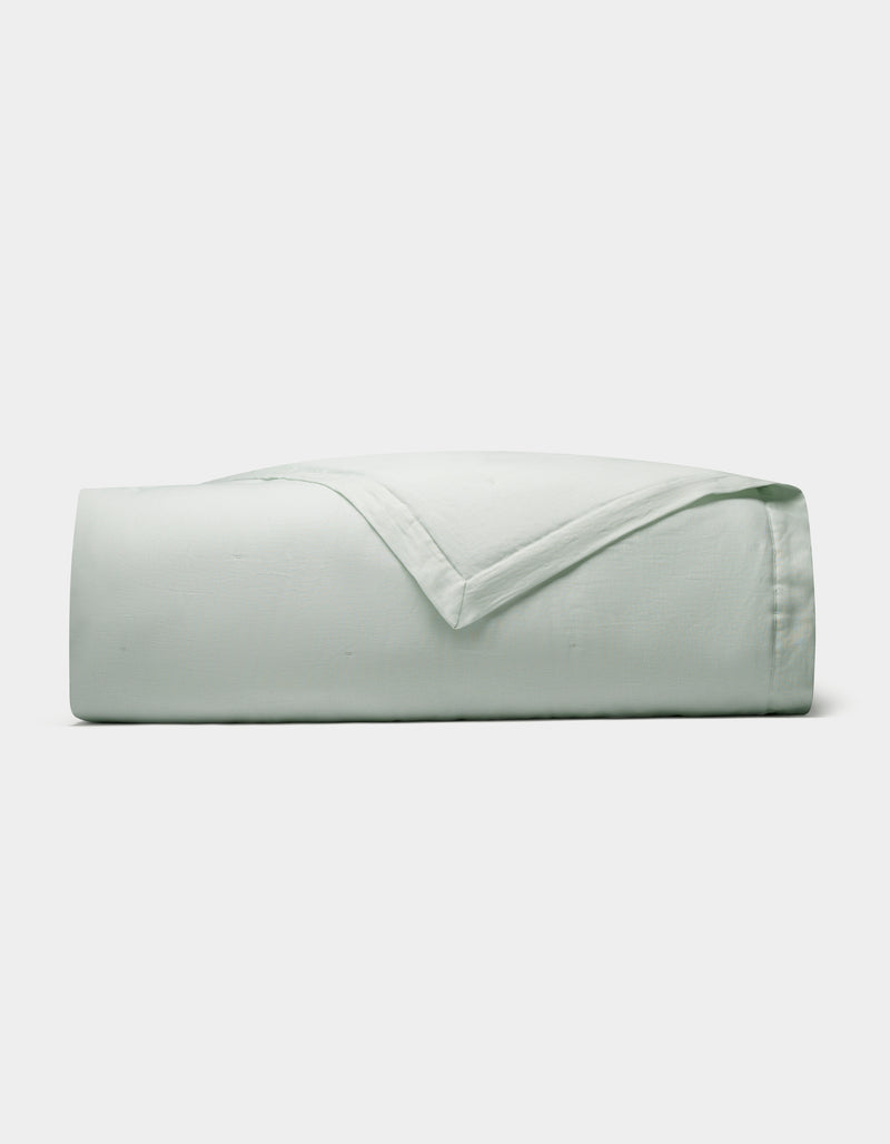 The Cozy Earth Linen Quilt, in a light green shade, is neatly folded and displayed against a plain white background.
