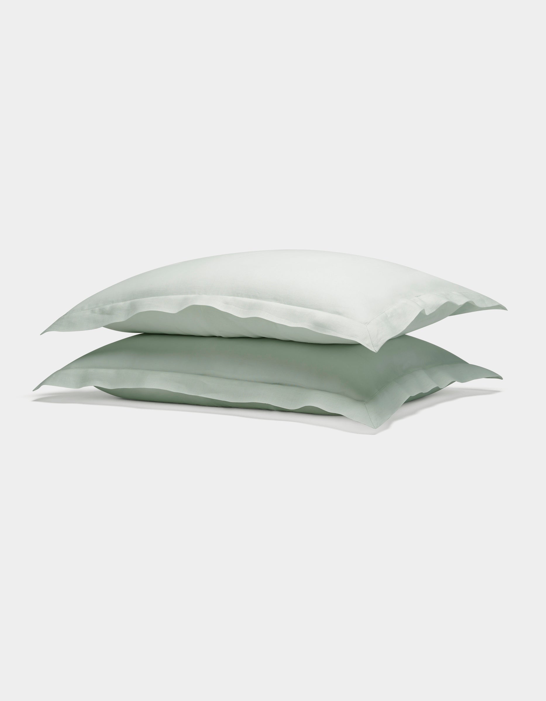Two Cozy Earth Linen Shams in light green are neatly stacked atop each other against a plain white background.|Color:Mist