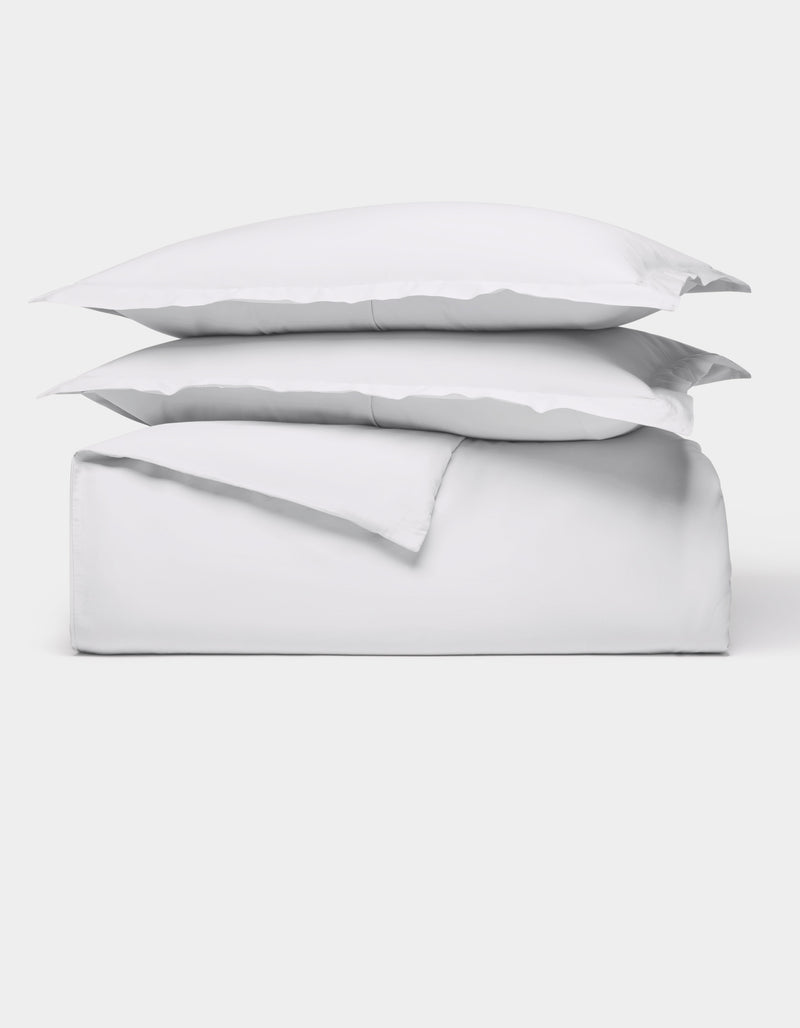 The Cozy Earth Soft-Wash Cotton Duvet Bundle features a neatly folded white sheet set with two stacked pillows, all displayed against a plain white background.