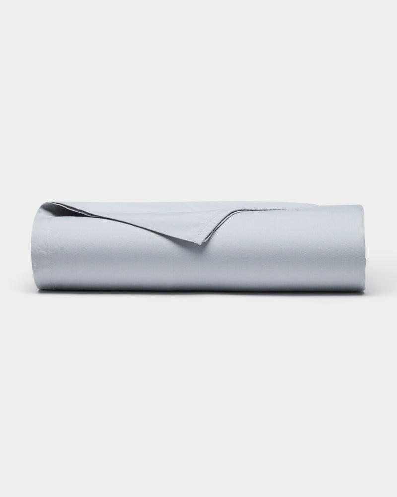 The Soft-Wash Cotton Sheet Set by Cozy Earth is shown neatly rolled up in light gray on a plain white background, with one corner gently lifted.