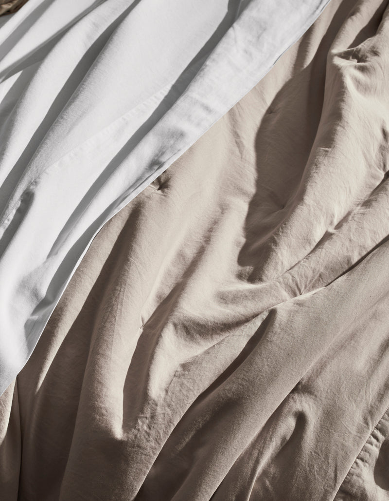 A close-up of the Cozy Earth Soft-Wash Cotton Quilt, showcasing its white and beige tones with gentle, natural light highlighting the soft texture and elegant folds.