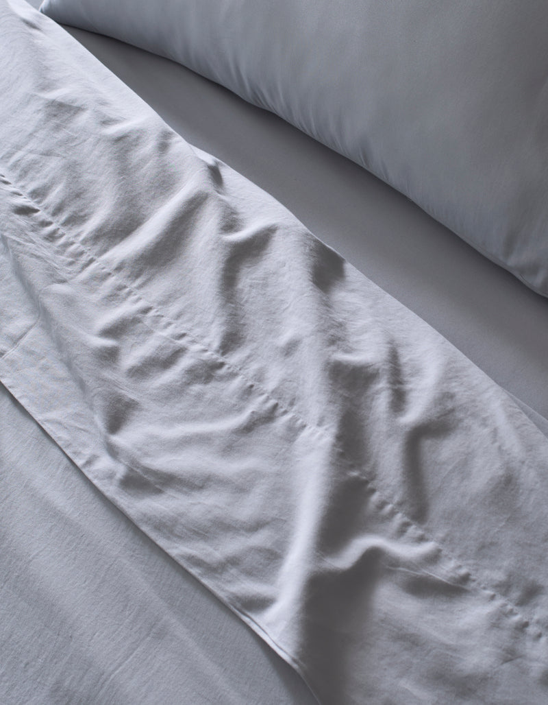Close-up of a neatly made bed featuring the Cozy Earth Soft-Wash Cotton Bedding Core Bundle in light gray, with softly wrinkled sheets and pillowcase hinting at recent use or adjustment.