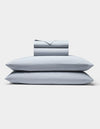 The Cozy Earth Soft-Wash Cotton Sheet Set, in light gray, includes two neatly stacked pillows and a matching folded sheet and pillowcase set, all displayed against a plain white background.|Color:Shore