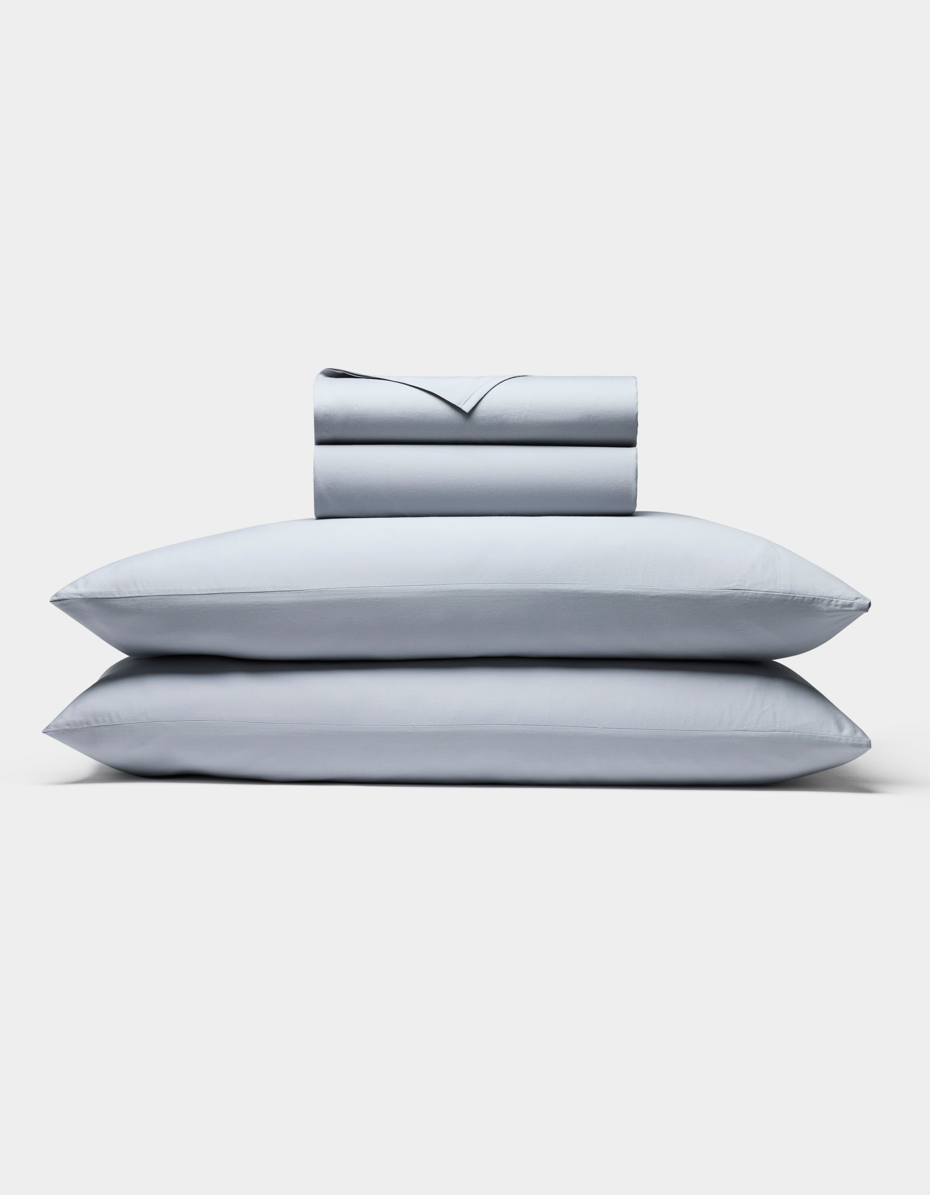 The Cozy Earth Soft-Wash Cotton Sheet Set, in light gray, includes two neatly stacked pillows and a matching folded sheet and pillowcase set, all displayed against a plain white background.
