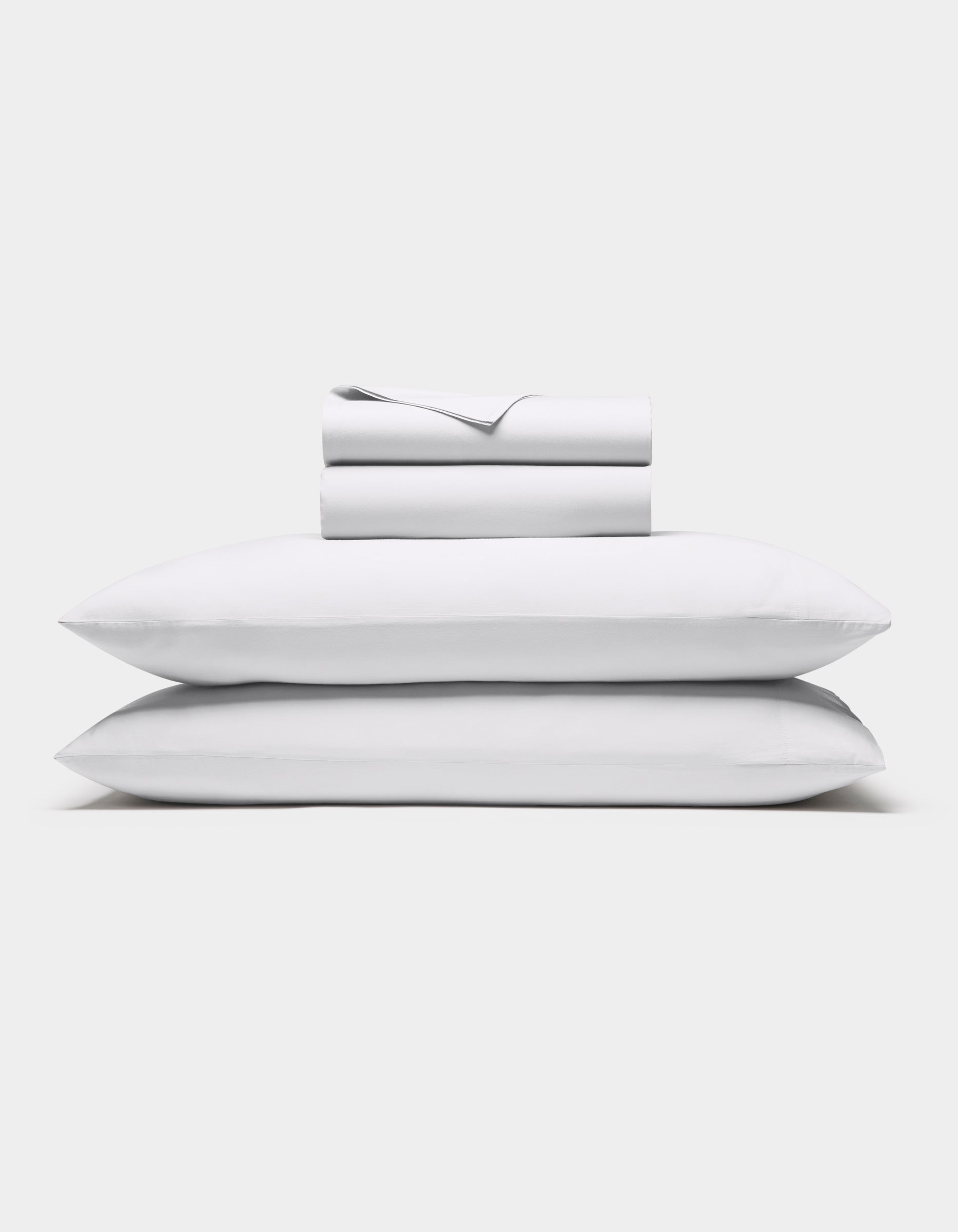 The Cozy Earth Soft-Wash Cotton Sheet Set in white, featuring a flat sheet, fitted sheet, and two pillowcases, is shown neatly stacked against a plain white background.