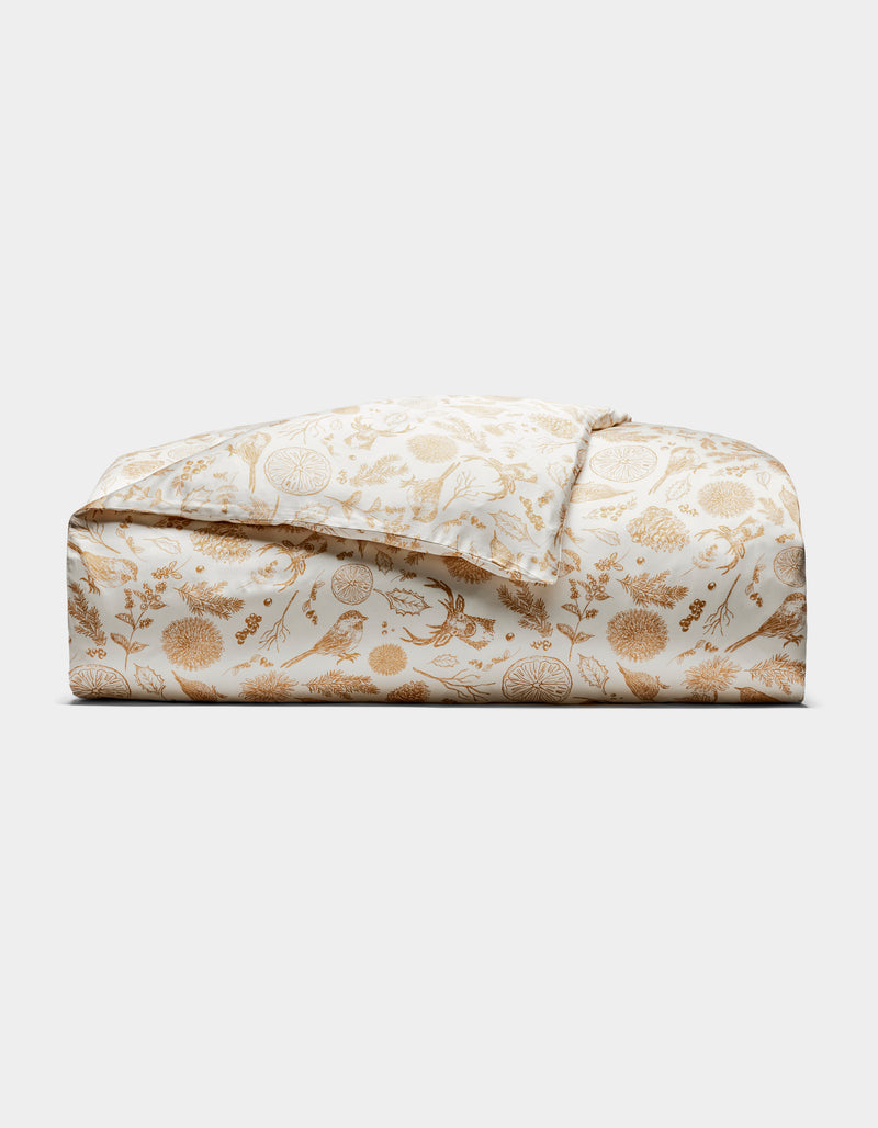 The Bamboo Duvet Cover by Cozy Earth is shown folded, featuring a white background with a gold floral and botanical print of detailed flowers, leaves, and birds, displayed against a plain white background.