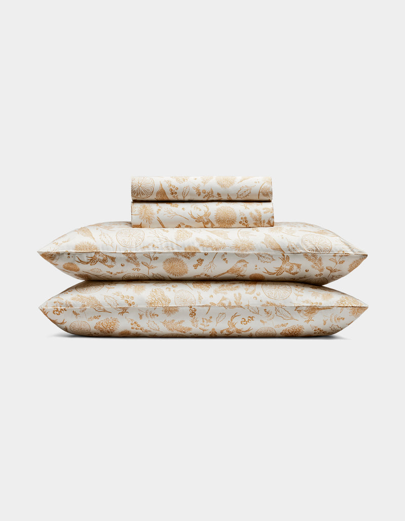 The Cozy Earth Bamboo Sheet Set includes two pillows and folded sheets with an intricate gold floral botanical pattern on a white background.