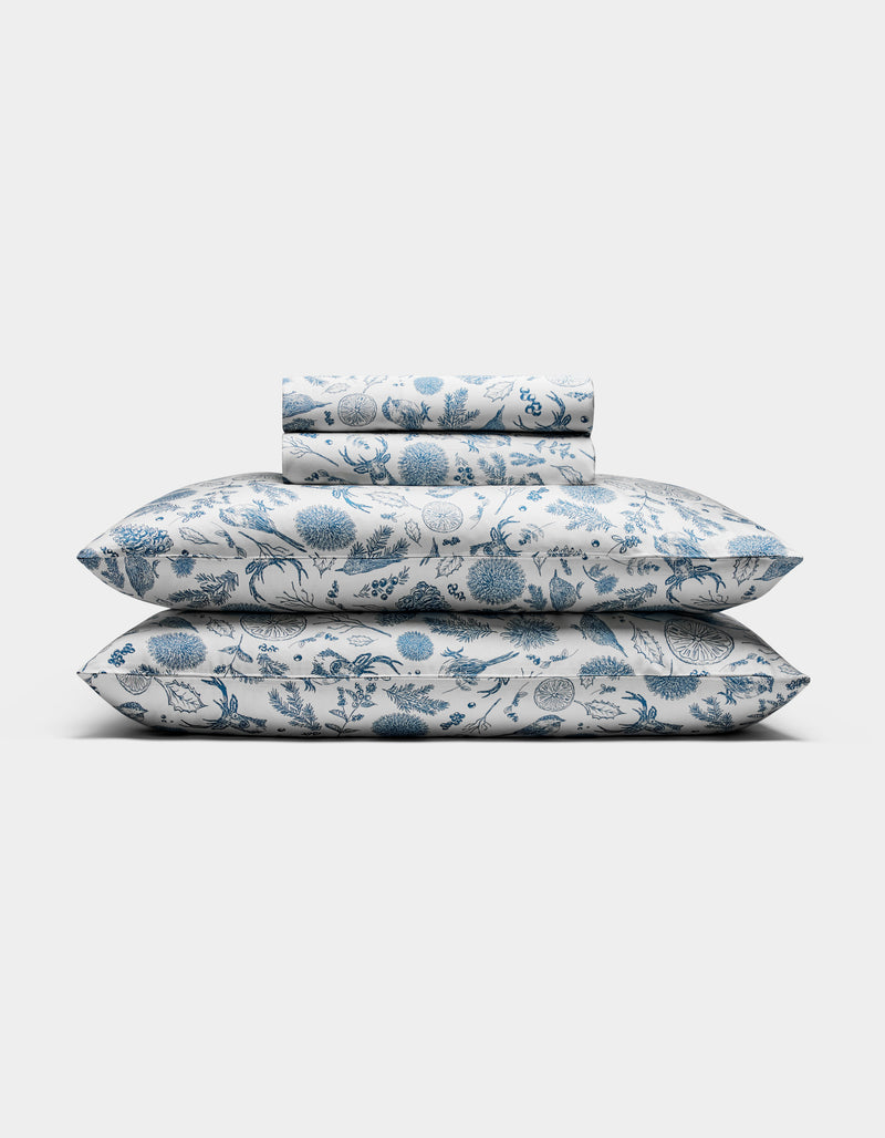 The Cozy Earth Bamboo Sheet Set, featuring pillowcases and sheets with a blue floral pattern on a white background, is neatly folded and displayed against a plain white backdrop.