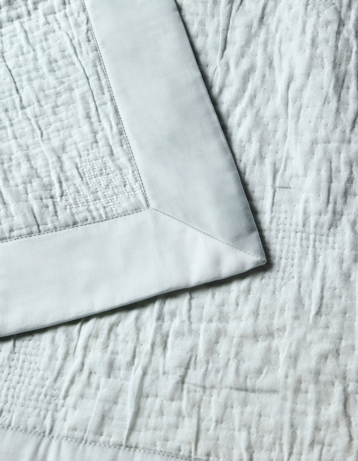 Close-up of the Cozy Earth Little Bee Matelasse Baby Blanket in light gray, showcasing its soft, textured fabric, visible stitched patterns, and a smooth satin border.