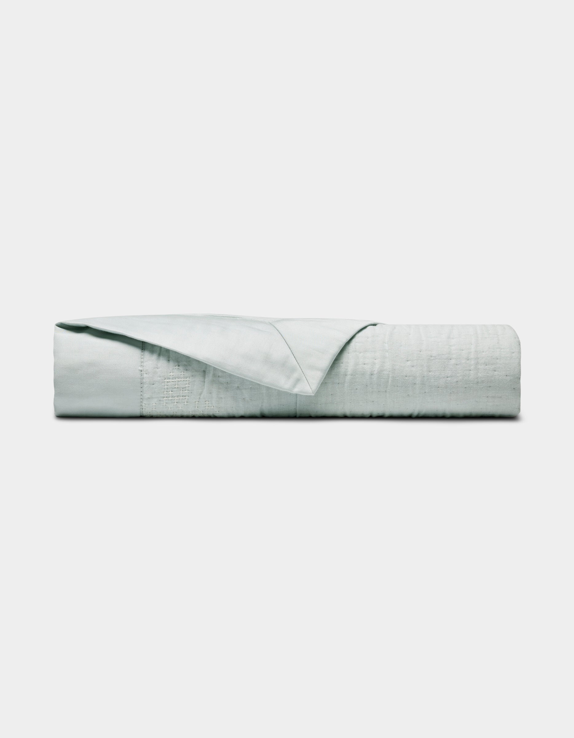 The Little Bee Matelasse Baby Blanket by Cozy Earth, shown neatly folded with one corner turned to reveal its smooth texture, is displayed in light gray or white against a plain white background.