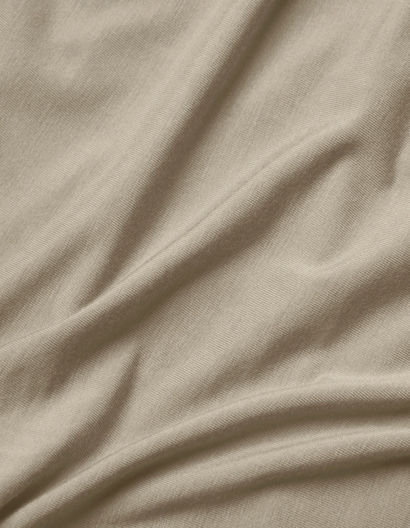 Close-up of Cozy Earth's Bamboo Jersey Flat Sheet in light beige, featuring soft, natural folds, gentle shadows, a smooth texture, and a subtle weave pattern.