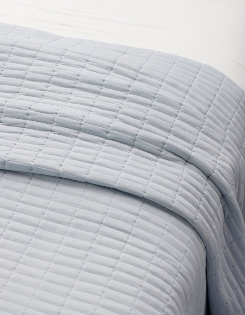 A close-up of a neatly made bed with the Cozy Earth Bamboo Jersey Quilt Bundle, featuring a light gray, square-patterned quilt layered over white sheets.