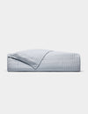 A neatly made bed displays the Cozy Earth Bamboo Jersey Quilt in light grey with a matching pillow, one quilt corner folded back, all set against a plain white background.|Color:Shore