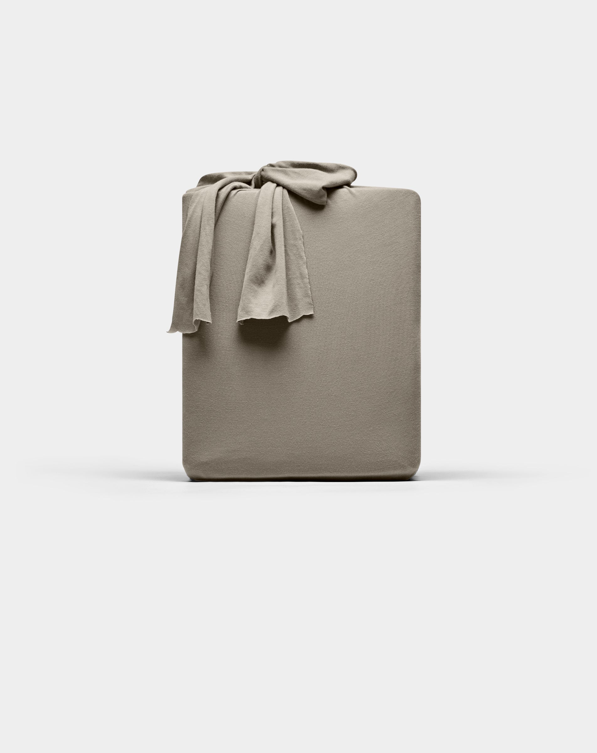 A taupe Cozy Earth Bamboo Jersey fitted sheet is neatly folded with one corner draped over the top, displayed against a plain white background.