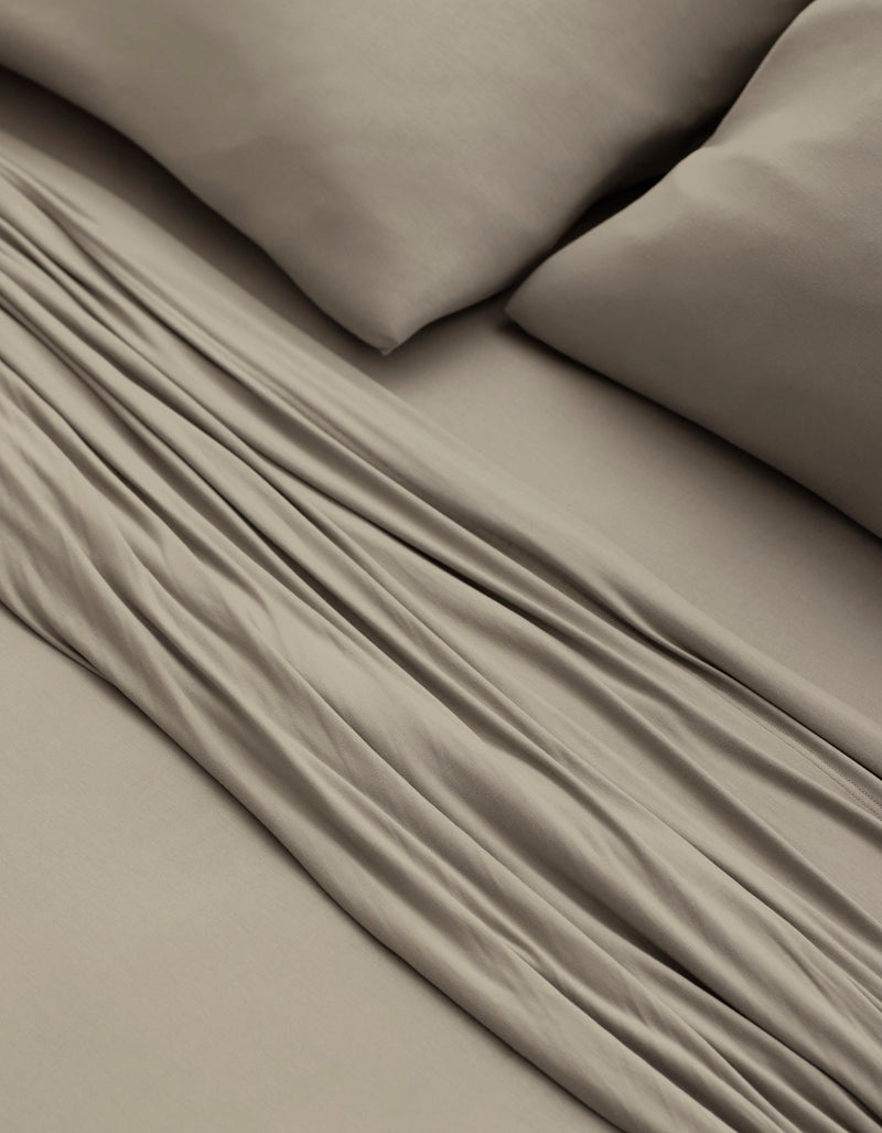A close-up of a bed made with Cozy Earth’s Bamboo Jersey Sheet Set in taupe, featuring two matching pillows and showcasing the soft fabric folds and smooth texture.