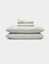 The Bamboo Sheet Set by Cozy Earth features neatly folded white sheets with subtle gray stripes, two stacked pillows, and additional folded sheets, all displayed against a plain white background.|Color:Classic Stripe in Laurel