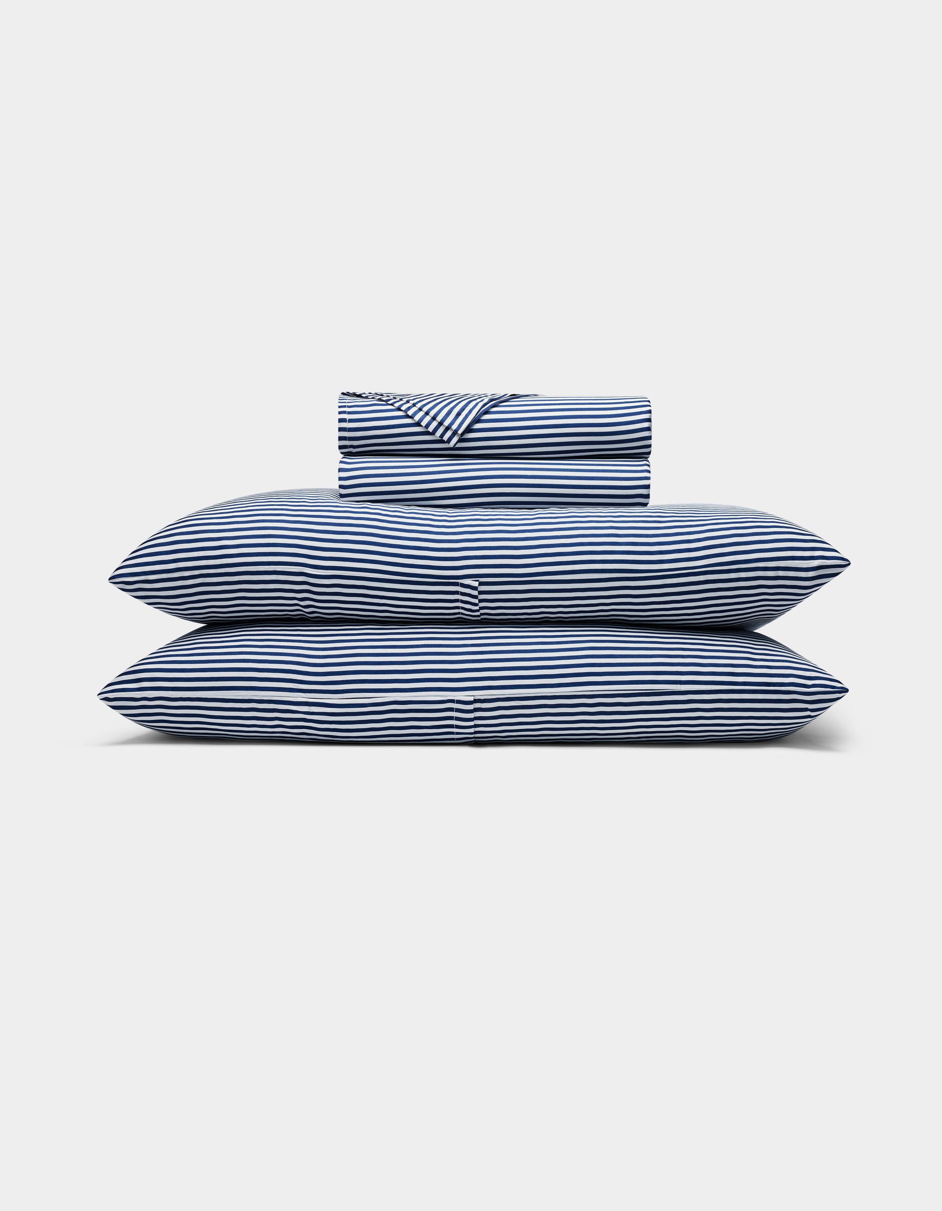 A neatly folded Bamboo Sheet Set by Cozy Earth, featuring blue and white stripes, with two pillows, a duvet, and a folded sheet stacked against a plain white background.|Color:Classic Stripe in Pacific