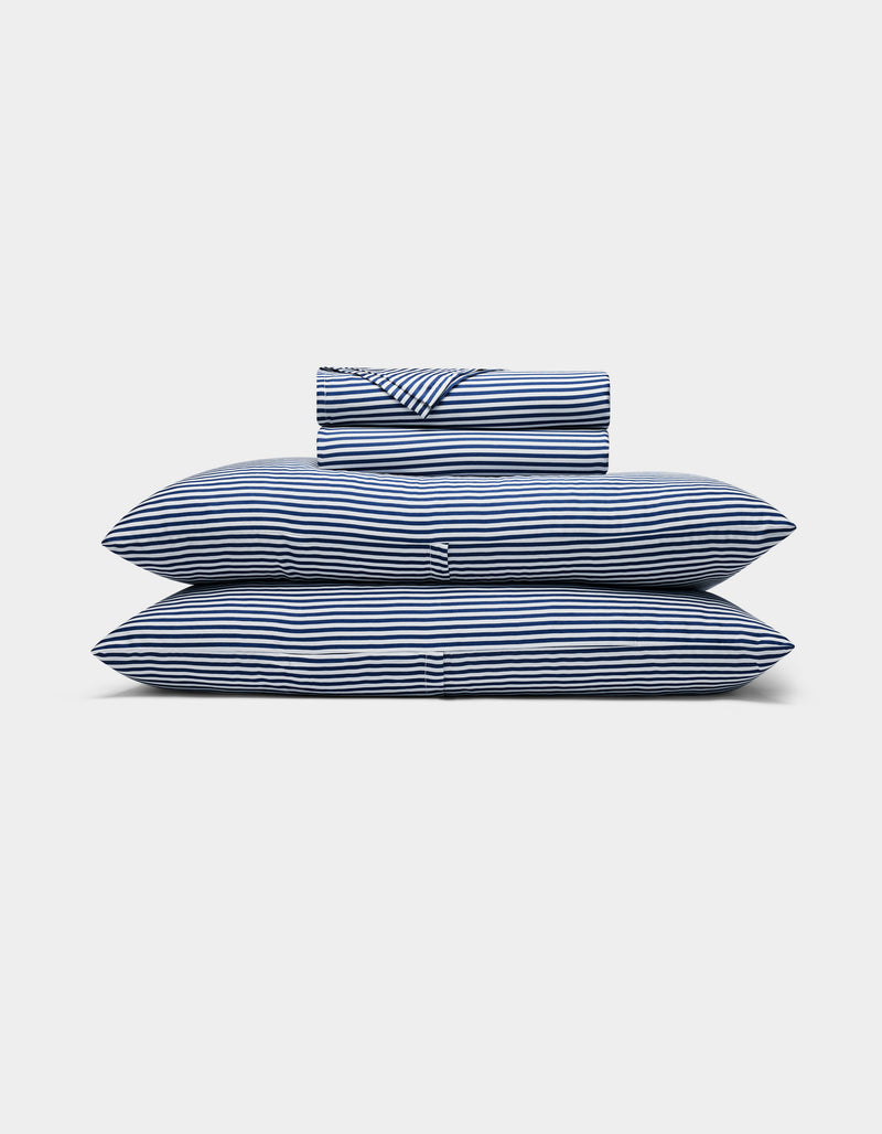 A neatly folded Bamboo Sheet Set by Cozy Earth, featuring blue and white stripes, with two pillows, a duvet, and a folded sheet stacked against a plain white background.