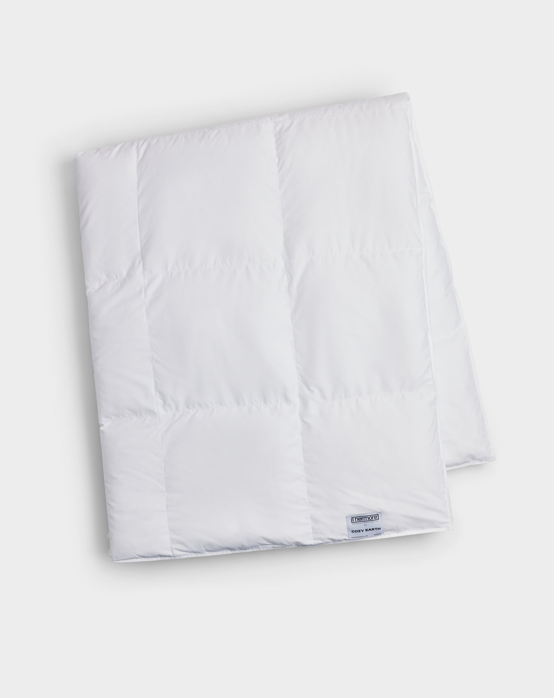 The Cozy Earth Down Alternative Throw, in white with stitched squares and a small corner label, is neatly folded and displayed on a plain light background.
