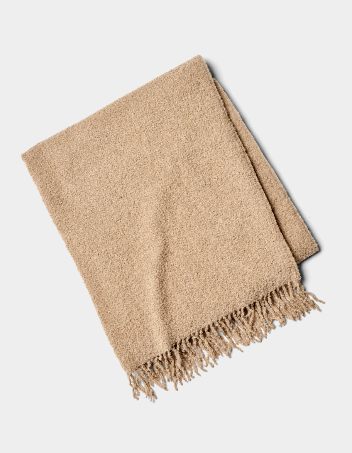 The Alpaca Boucle Throw by Cozy Earth is a beige blanket with a soft, textured surface and fringed edges, shown folded on a plain white background.|Color:Sandalwood