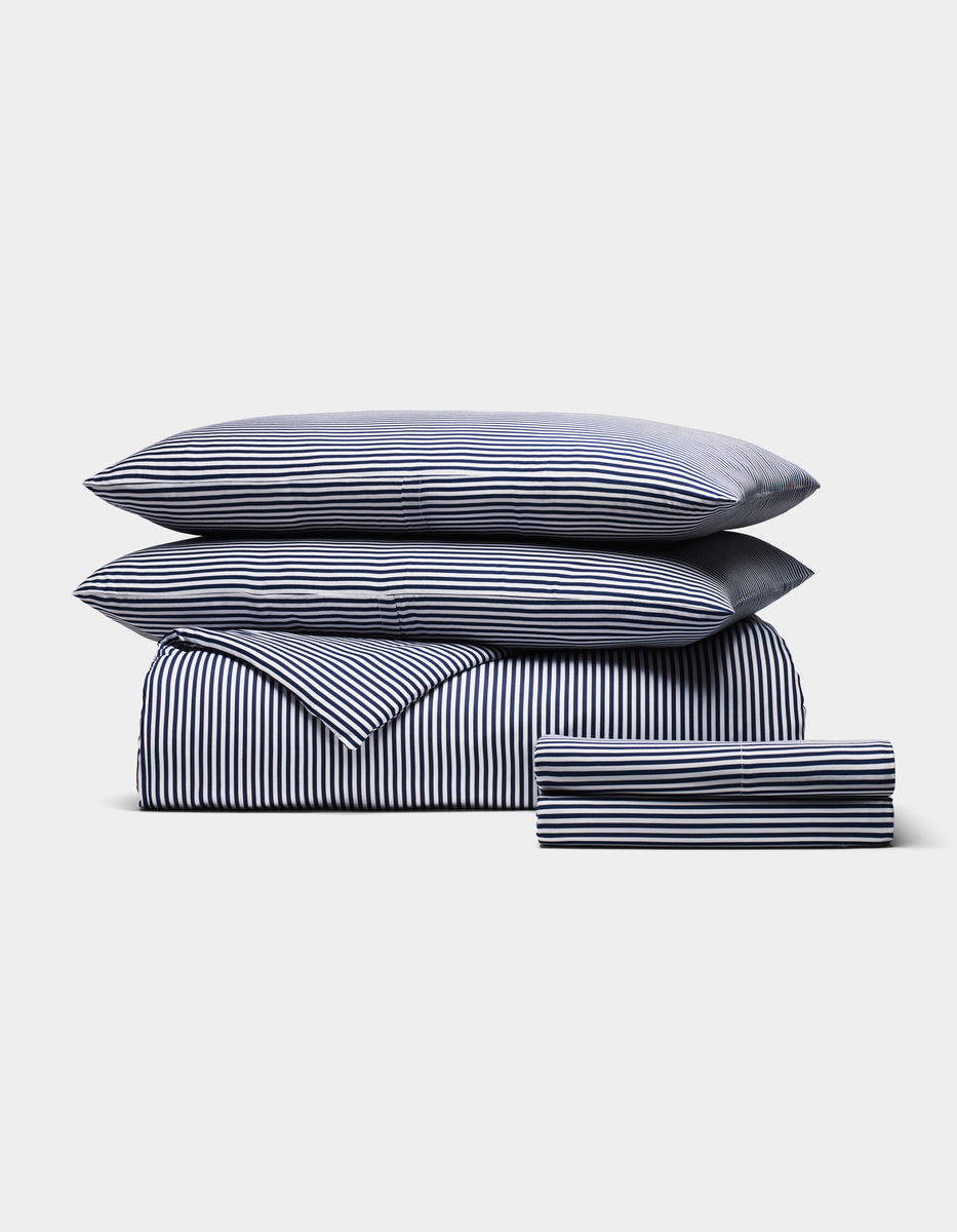 The Cozy Earth Bamboo Bedding Deluxe Bundle, featuring two pillows, a duvet, and sheets with navy and white vertical stripes, is neatly folded and displayed against a plain light background.