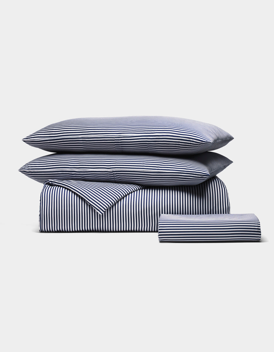 The Cozy Earth Bamboo Bedding Essential Bundle, featuring two pillows, a duvet, and a folded sheet in blue and white stripes, is neatly stacked on a plain white background.|Color:Classic Stripe in Pacific