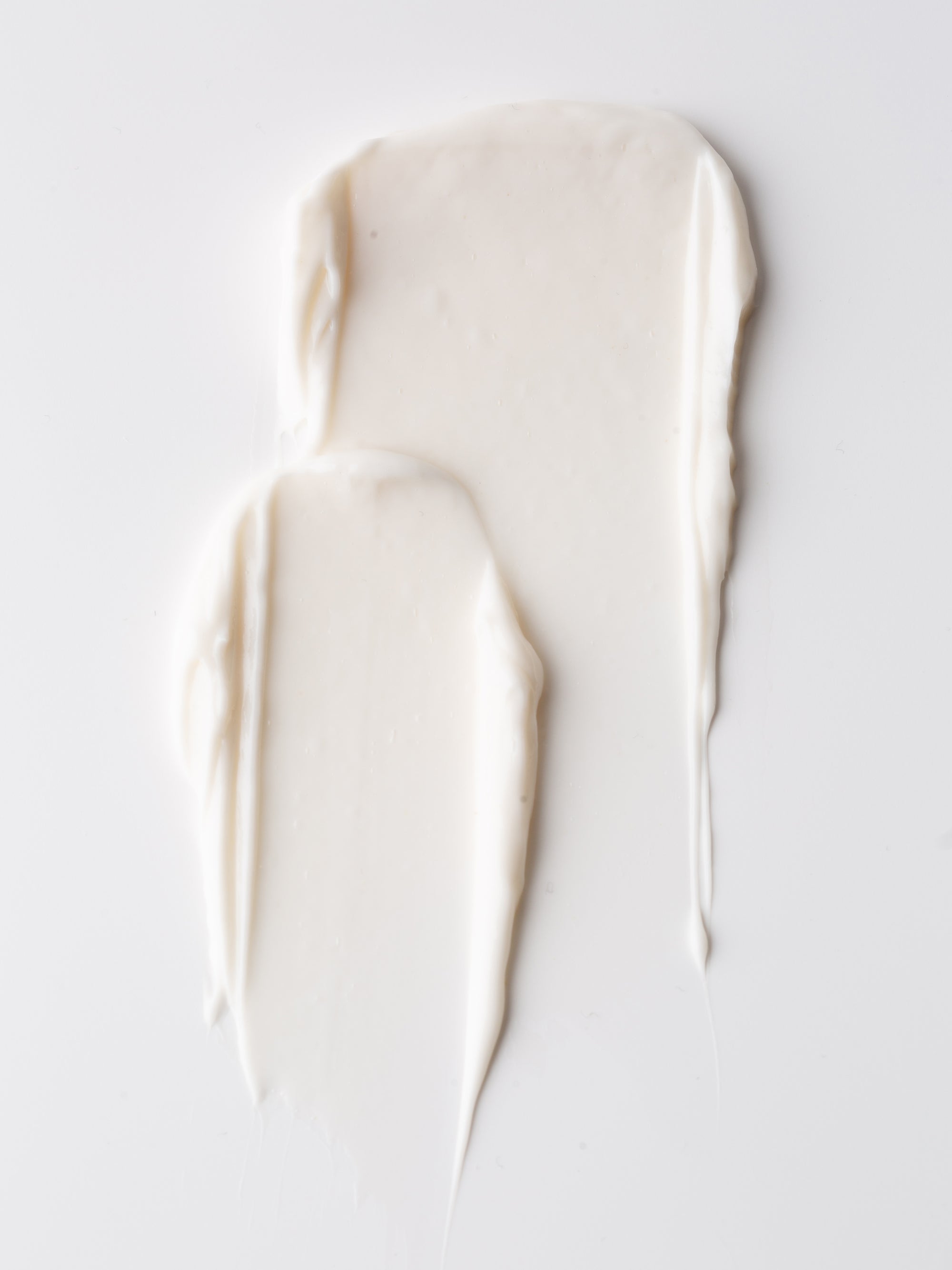 Two swipes of Fount Society Intro Kit moisturizer by Cozy Earth are smeared on a smooth white surface, creating soft, textured, elongated shapes.