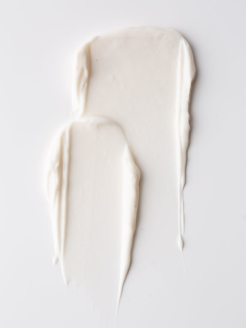Two textured swatches of Cozy Earth Body Butter are spread on a clean, white surface. The Body Butter has a smooth, silky appearance with some visible ridges and lines from the spreading motion.