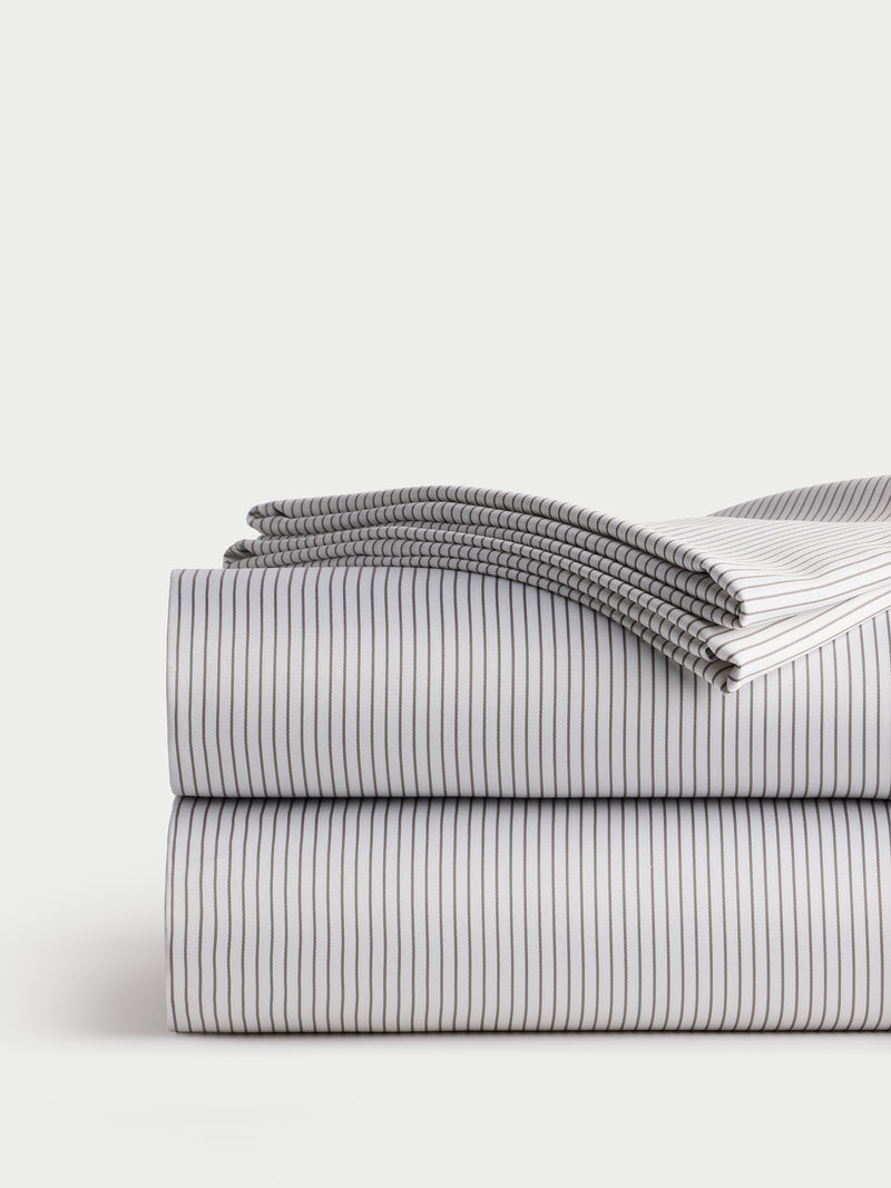 A neatly folded stack of Cozy Earth's Bamboo Sheet Set, featuring a clean white design with thin black stripes set against a neutral background. The top sheet is partially unfolded, displaying the elegant striped pattern.